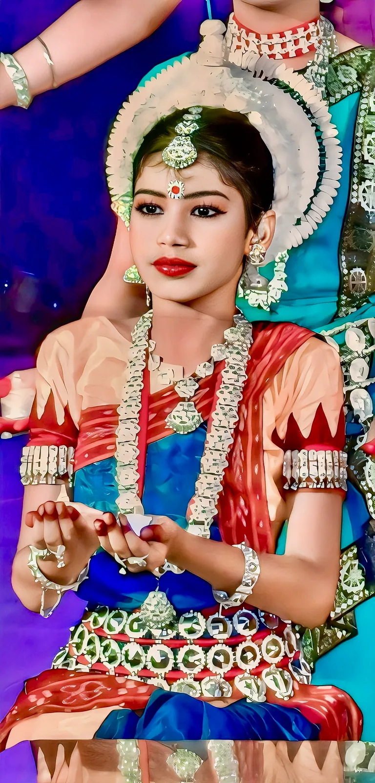 Two young Odissi dancers in a studio, one kneeling and one standing with hands joined