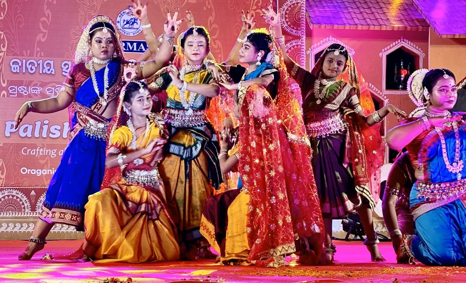Seven dancers in a closing formation on stage beneath the International Performing Arts Festival, Puri 2024 banner